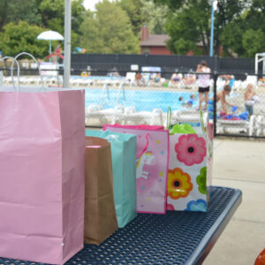 Birthday present bags lined up on a picnic table out by the pool