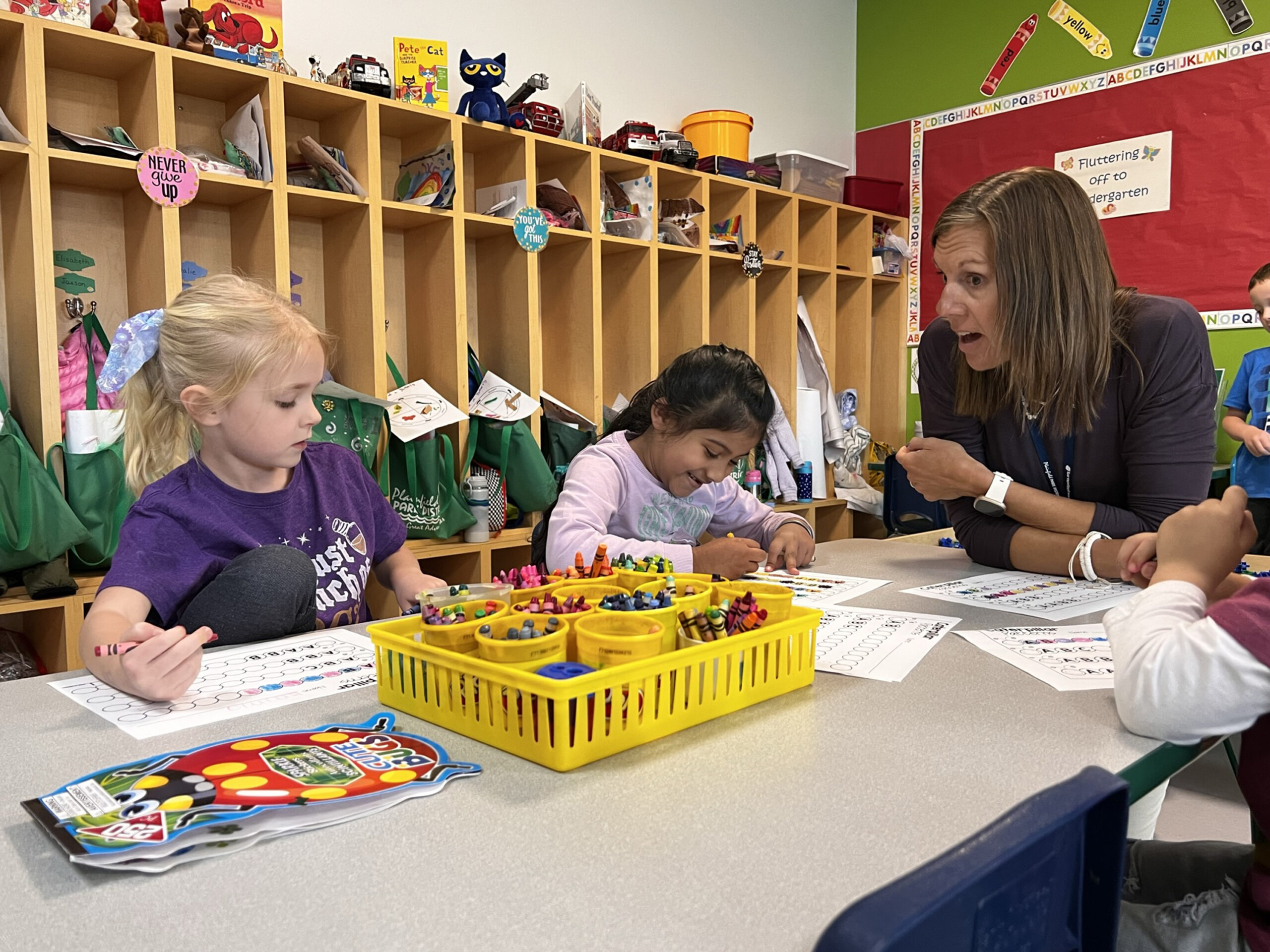 Preschool teacher sitting at a table with students coloring